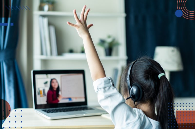 A young girl attending an online classroom session raises her hands to show participation.