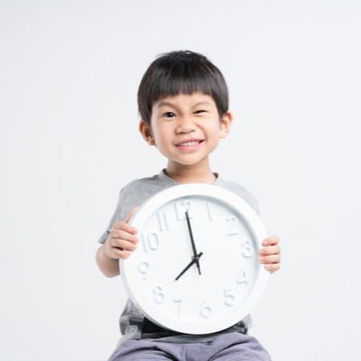 Young schoolboy holding a clock with a mischievous smile.