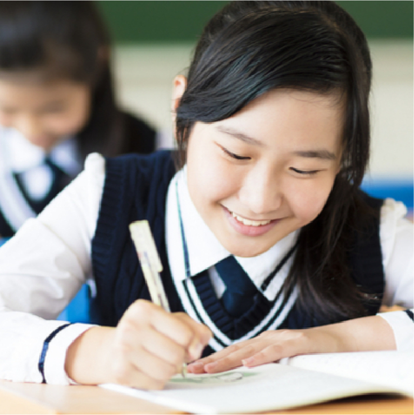 Close-up portrait of a smiling primary school student sitting at her desk and writing in her notebook.