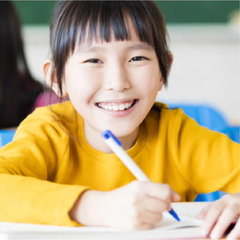 Close up portrait of smiling primary school student sitting at her desk and writing in her notebook.