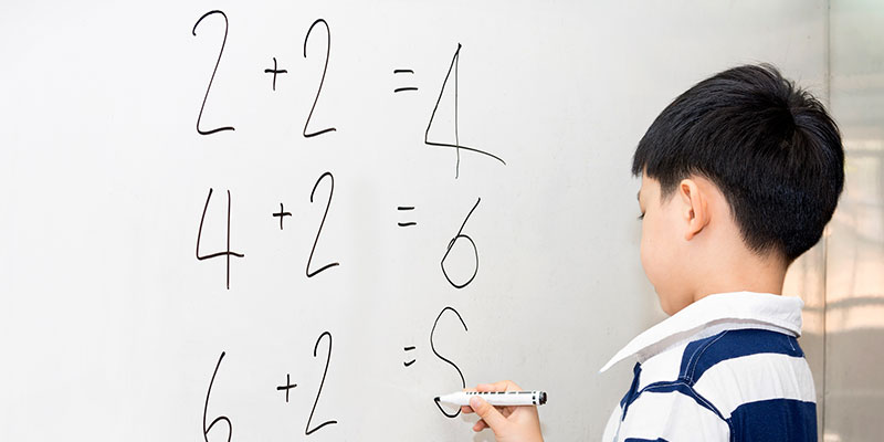 In a classroom setting, a boy is doing math calculations on the whiteboard.