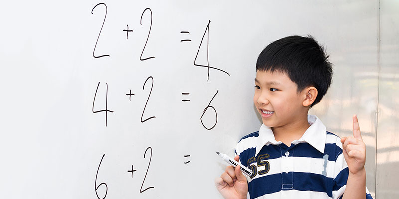 A young boy has a math exercise on the whiteboard with a blank answer, thinking about it.
