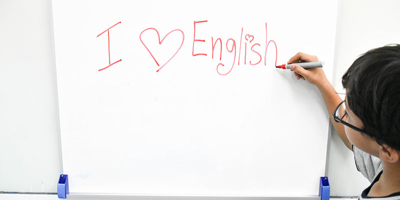On a whiteboard, a young boy is writing I love English.