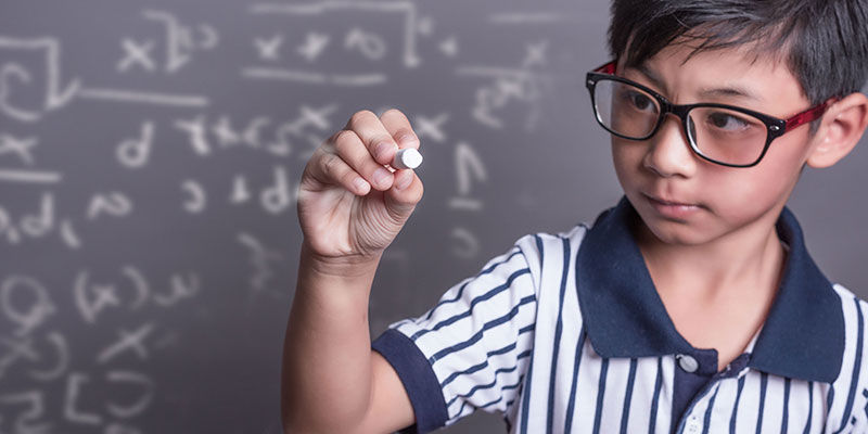 A young schoolboy with chalk in his hand in front of the blackboard solves the math problems.