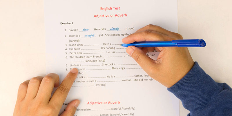 Hands holding a blue pen and practising and taking the PSLE English test. Practising and revising English.