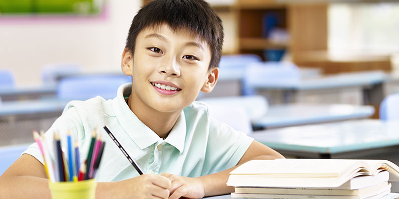 A smiling boy student taking a PSLE mock exam in a classroom.