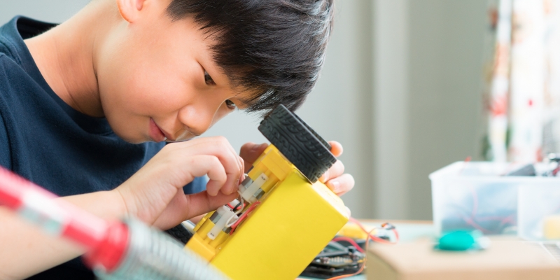 Close-up shot of a schoolboy working on a robotic project and working with circuits, OLED, wires, and computer chips.