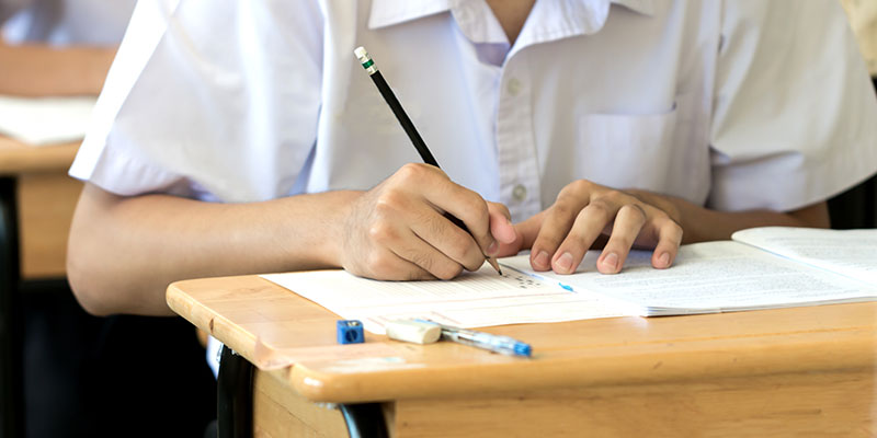 A student is giving a PSLE English exam sitting comfortably on the desk. The exam booklet with other writing materials is available on the table.