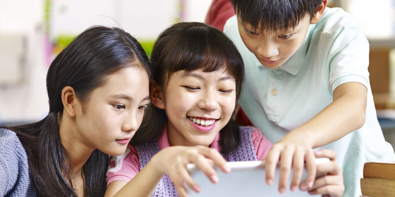 A group of three students are looking at the tablet and happily discussing about a reading topic for the PSLE English oral exams.