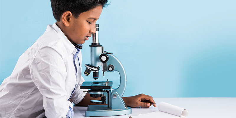 A small schoolboy is looking into a microscope for his PSLE science learning.