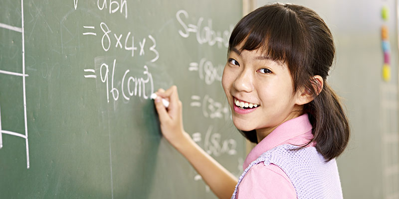 A happy school student is seen writing maths formulae on the board.
