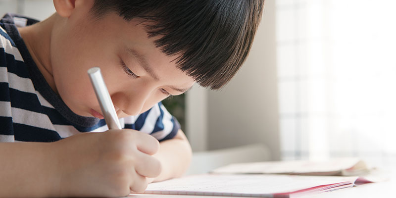 A close-up shot of a schoolboy doing homework in the notebook.