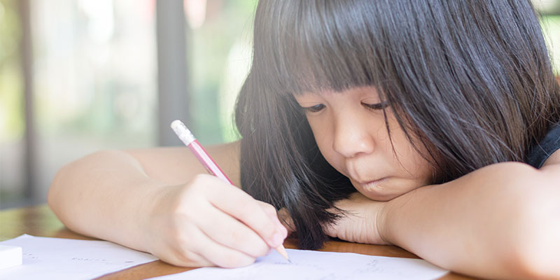 An Asian girl is solving PSLE question papers with a pen.
