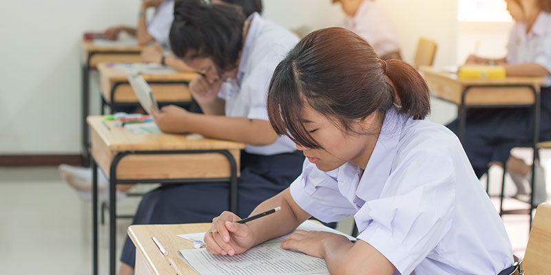 A group of students, taking an examination with a question paper and answer sheets in their hands.