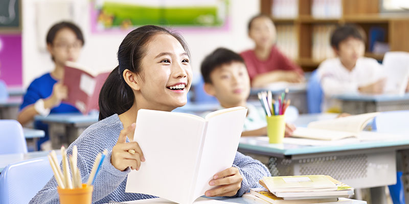 An Asian elementary school student smiling in a classroom.