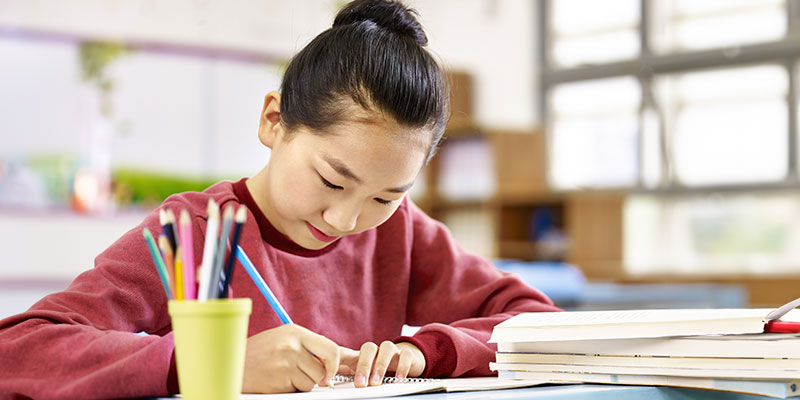 An Asian primary school girl writing in a classroom.