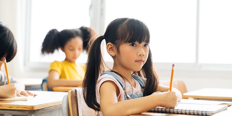 An Asian schoolgirl sitting in class with a pencil illustrates PSLE preparation.